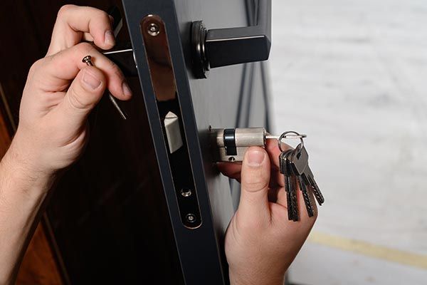 A person is fixing a door lock with a screwdriver and keys.
