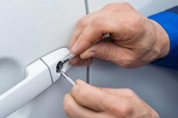 A person is using a screwdriver to fix a car door lock.