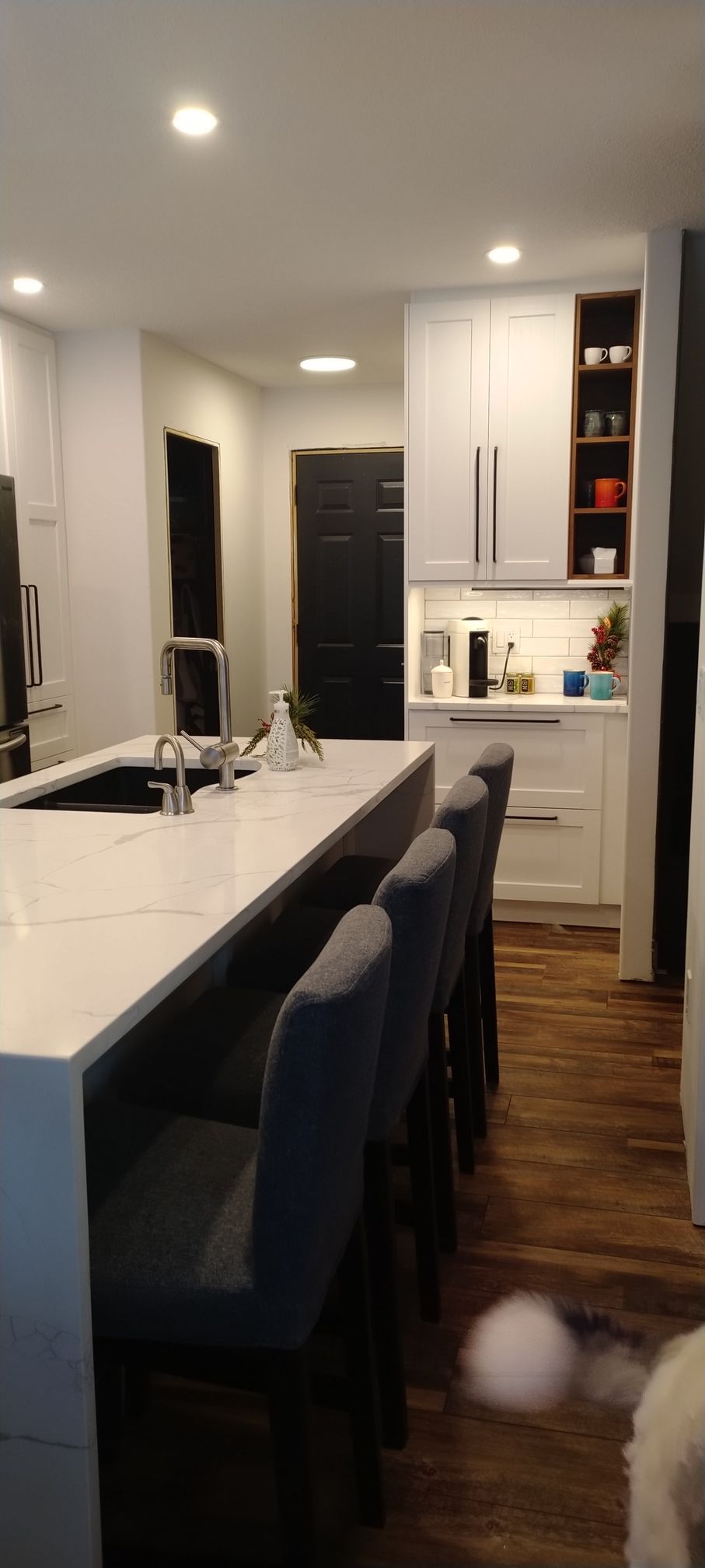 A kitchen with a large island , stools , a sink and a refrigerator.