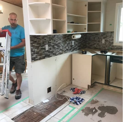 A man in a blue shirt is carrying a ladder in a kitchen