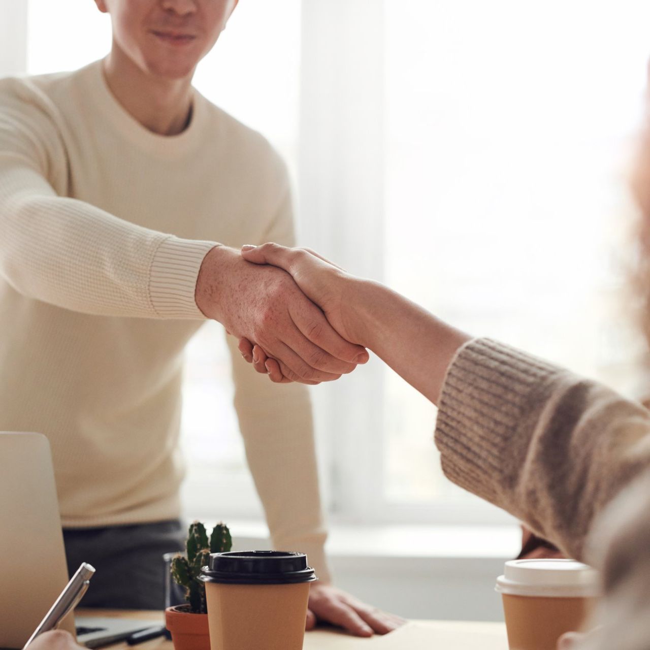 A man and a woman are shaking hands at a table.