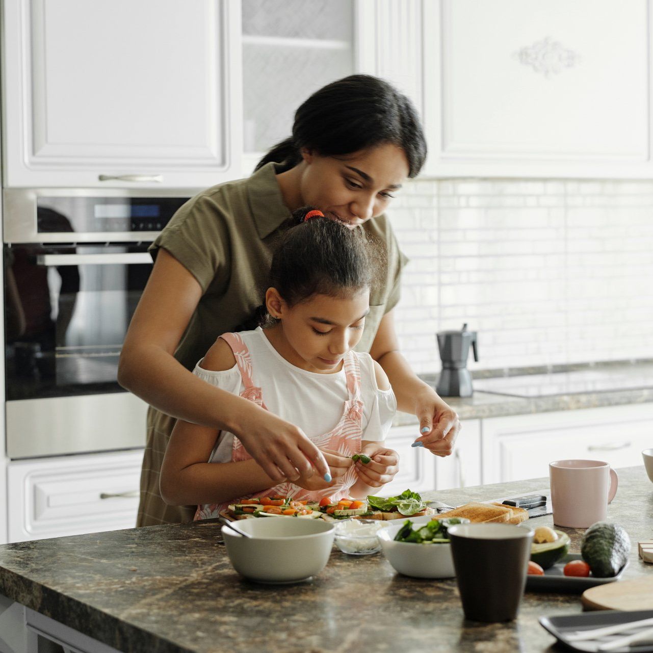 A woman and a little girl are preparing food in a kitchen.