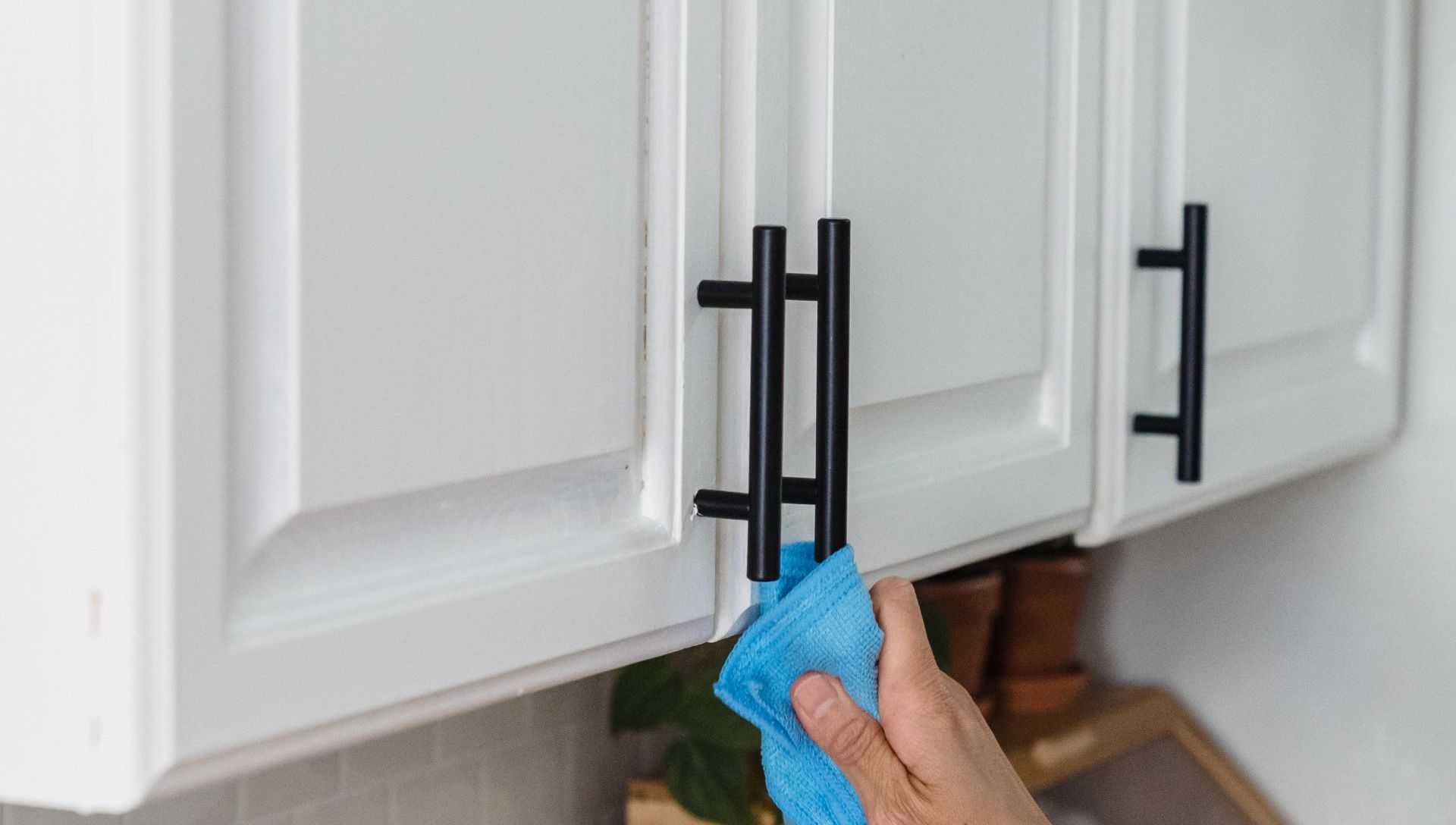 A person is cleaning a kitchen cabinet with a blue cloth.