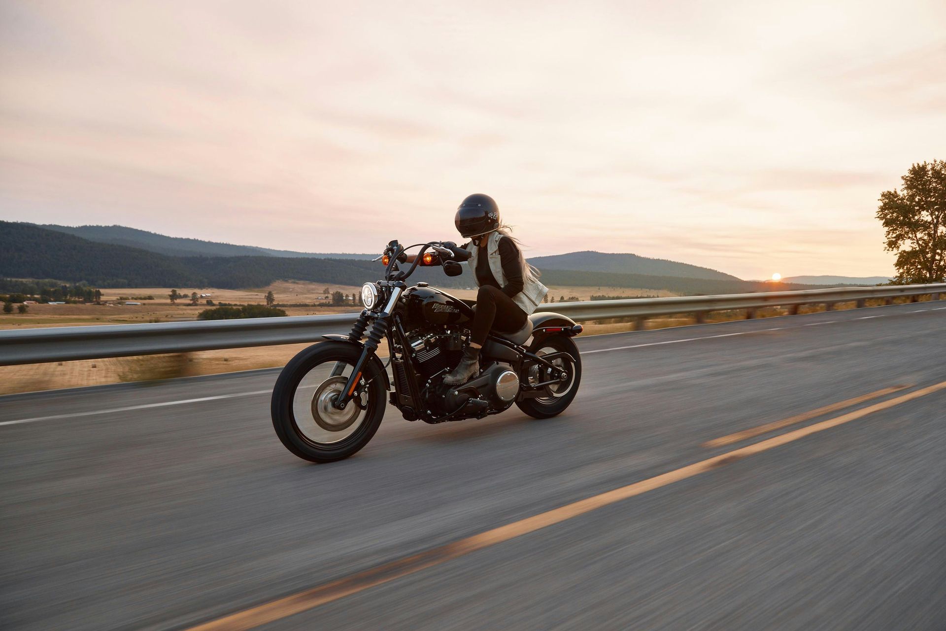 Motorcyclist on a black motorcycle riding on a road with a scenic background at sunset.?