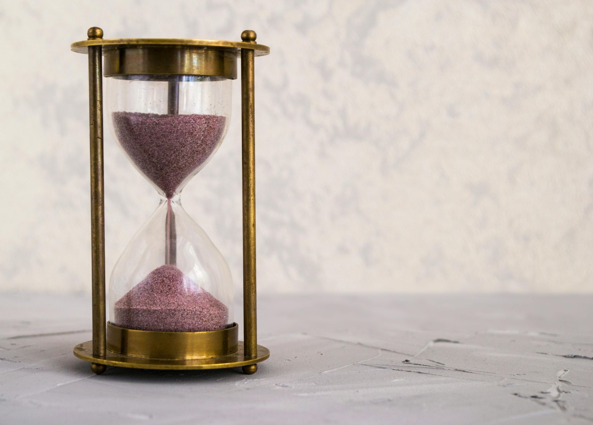 Vintage brass hourglass with purple sand on a white surface