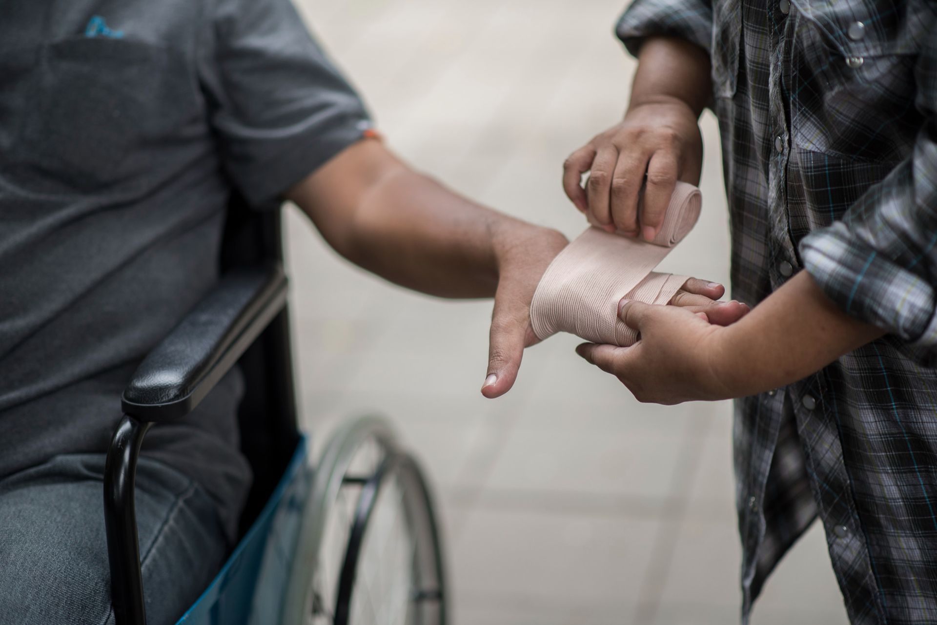 Person wrapping another person's hand with a bandage beside a wheelchair