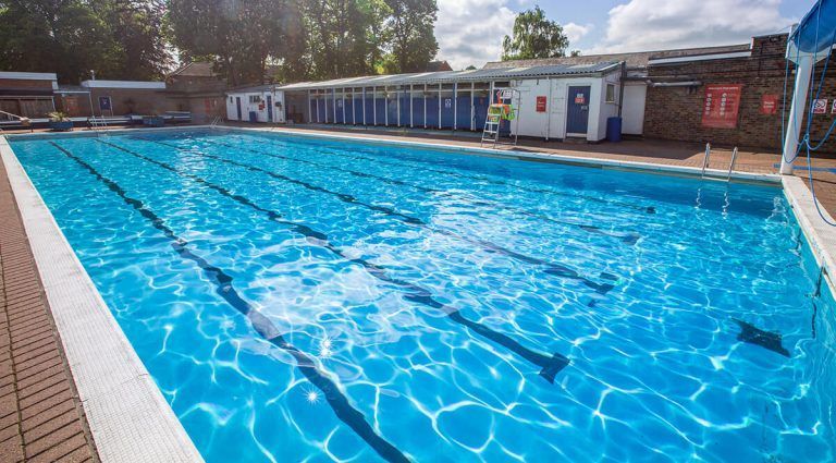 A large swimming pool filled with blue water and a building in the background.