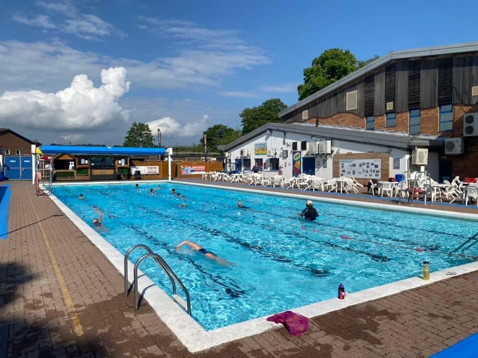 A large swimming pool with people swimming in it and a building in the background.