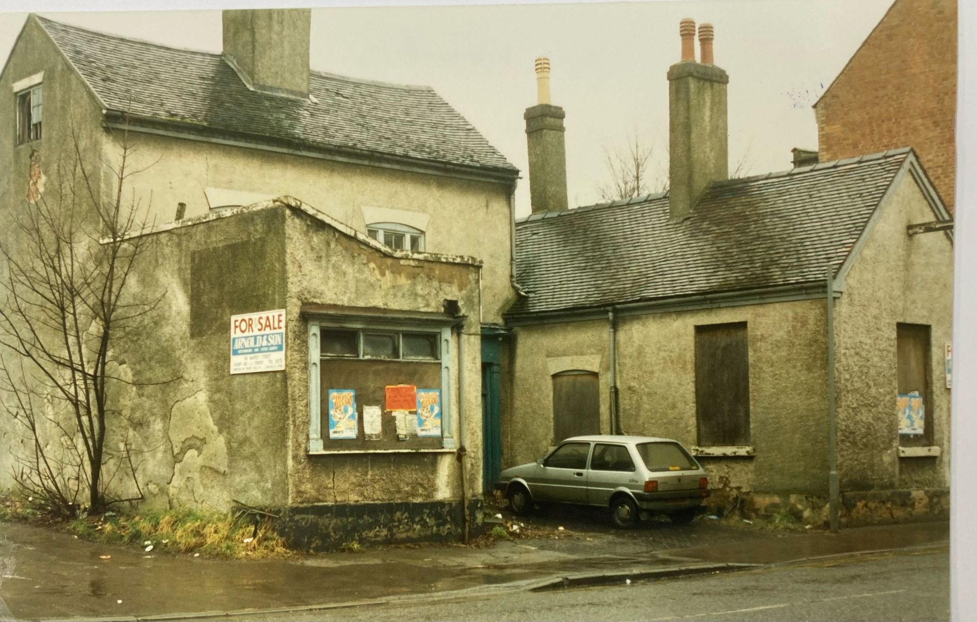 A car is parked in front of a building that says it is for sale