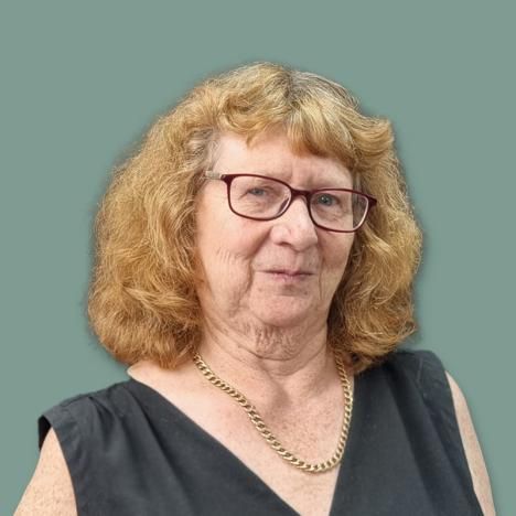 Jane Boyer wearing glasses and a necklace is standing in front of a green background.