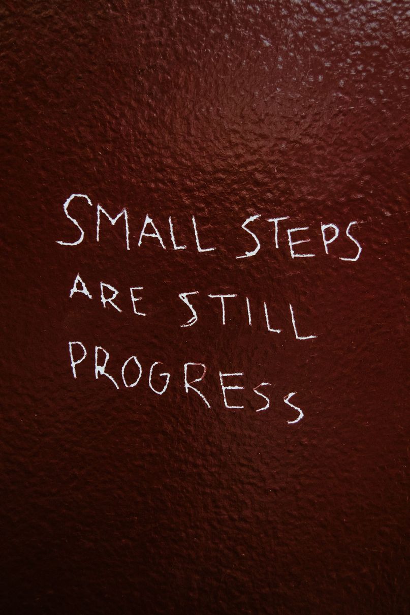 Handwritten white text on a dark background: “Small steps are still progress.”