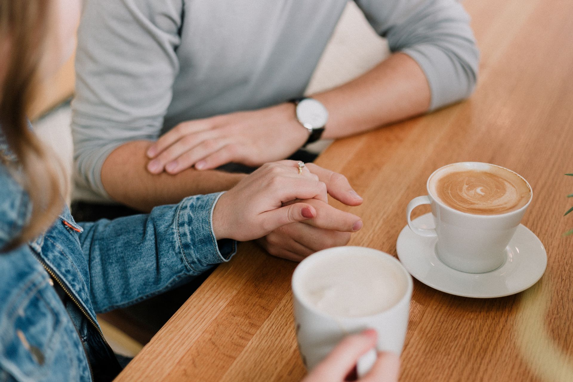 Two people holding hands at a café table with coffee cups