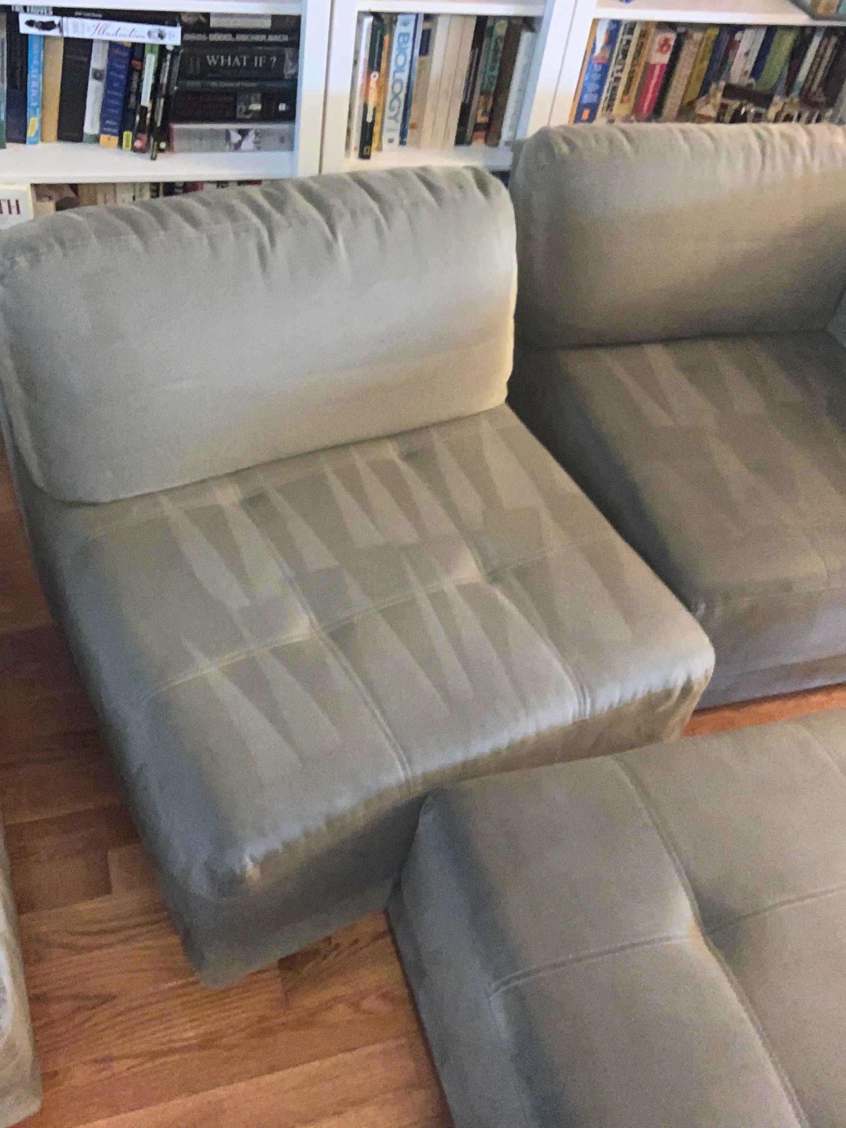 A living room with a couch , chair and ottoman in front of a bookshelf filled with books.