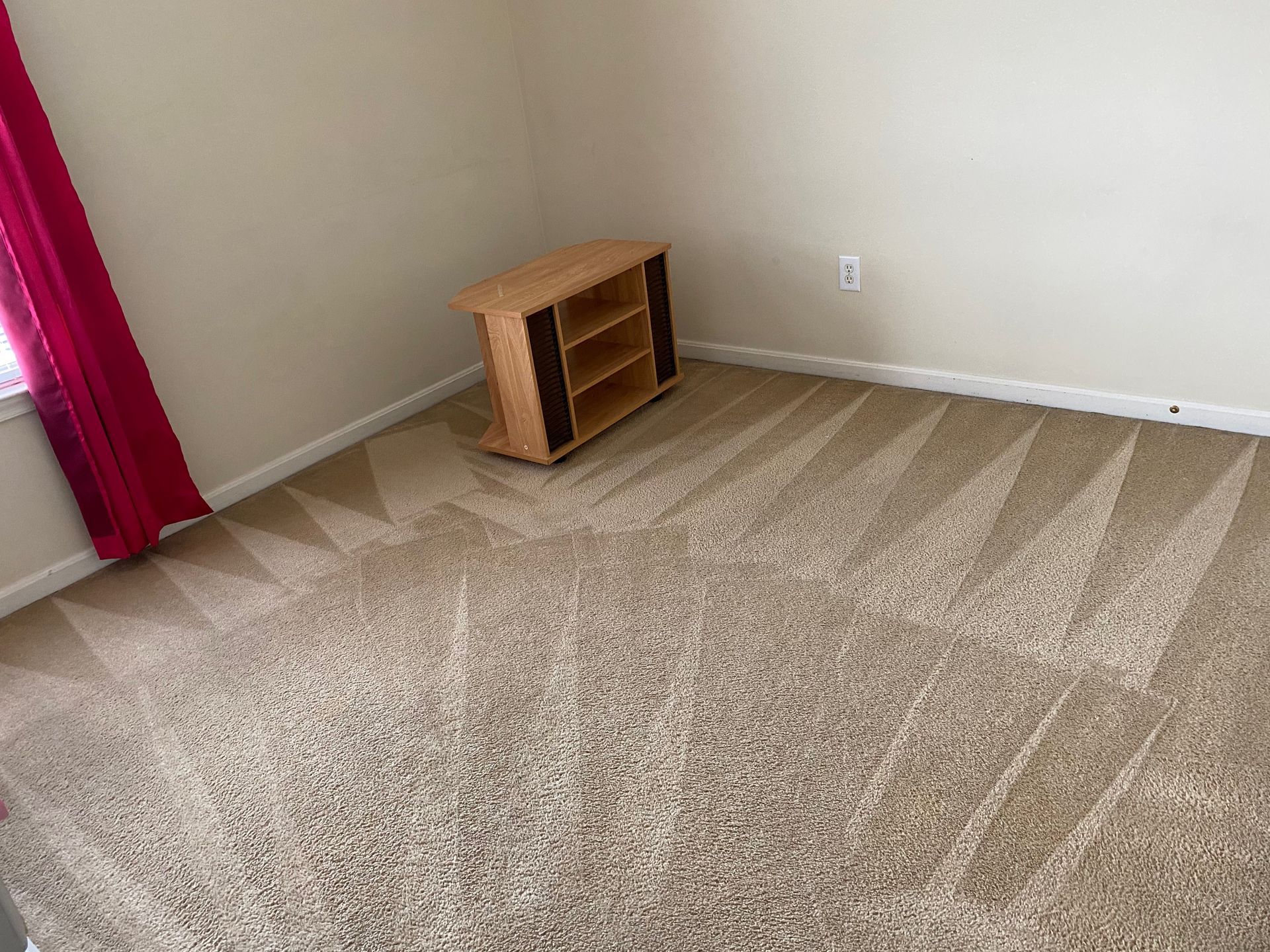 An empty room with a carpeted floor and a wooden entertainment center.