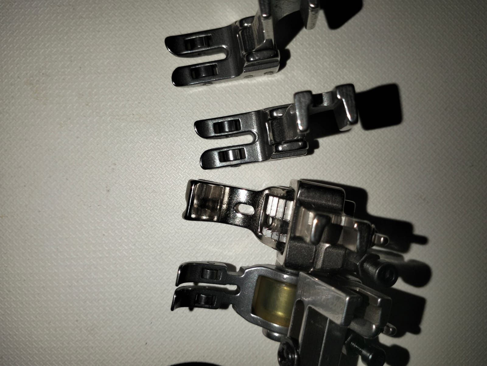 Tres prensatelas para máquina de coser de color plateado sobre una superficie blanca.
