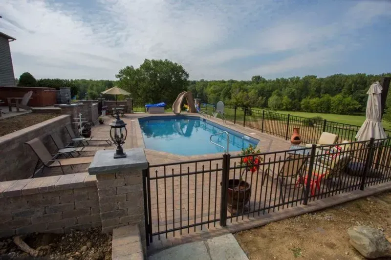 A large swimming pool is surrounded by a fence and chairs.
