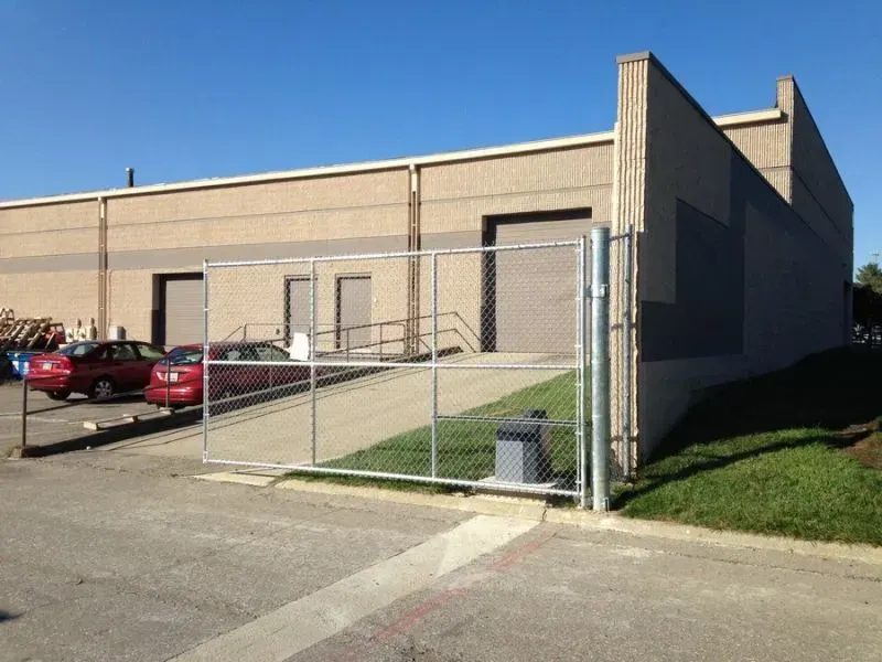 A chain link fence surrounds a building with cars parked in front of it