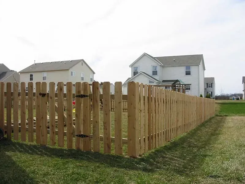 A wooden fence surrounds a grassy field in front of a house