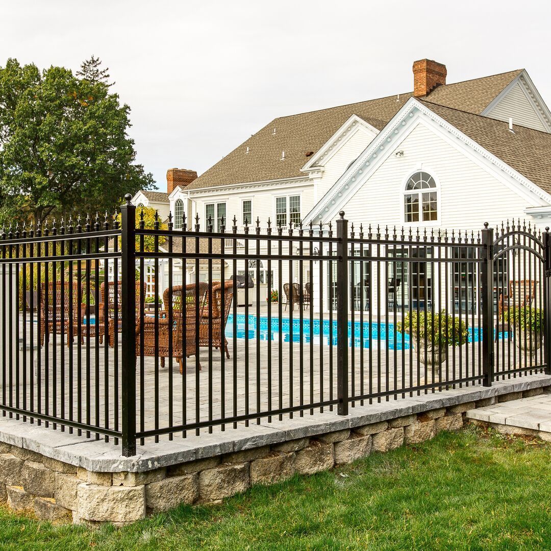 A large white house with a swimming pool behind a black fence.