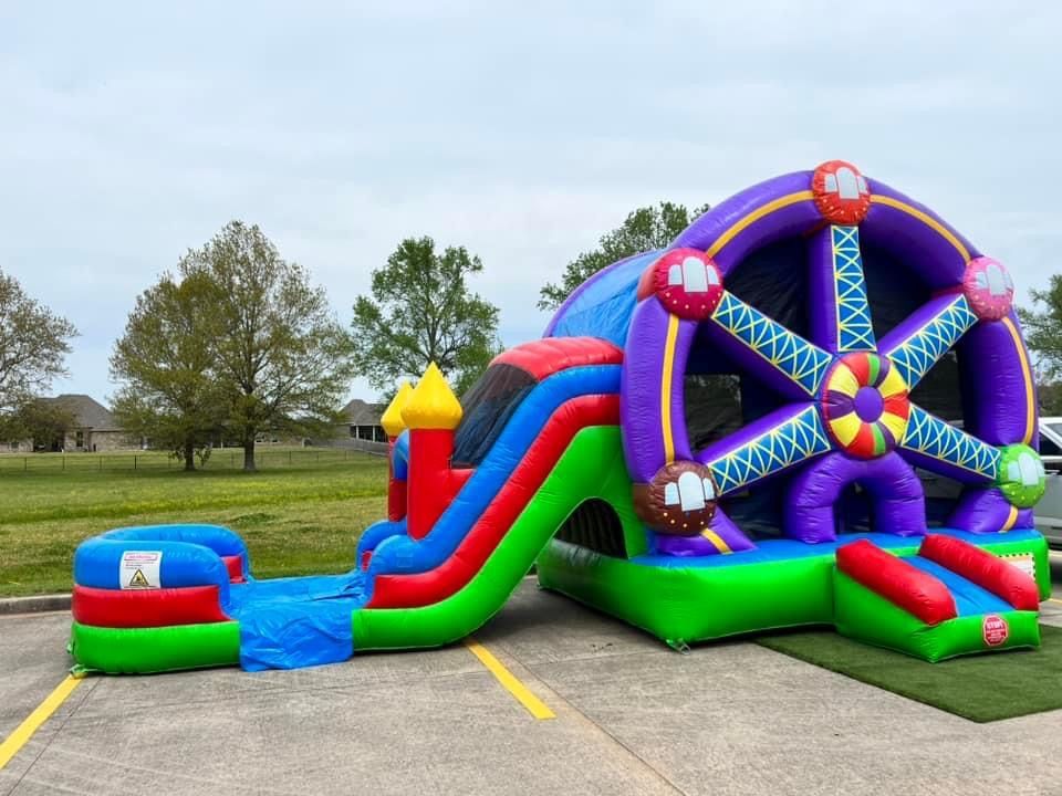 A ferris wheel bouncy house with a slide and a water slide is parked in a parking lot.