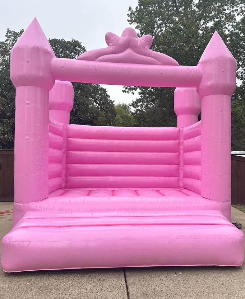 A pink bouncy castle with a crown on top is sitting on a sidewalk.