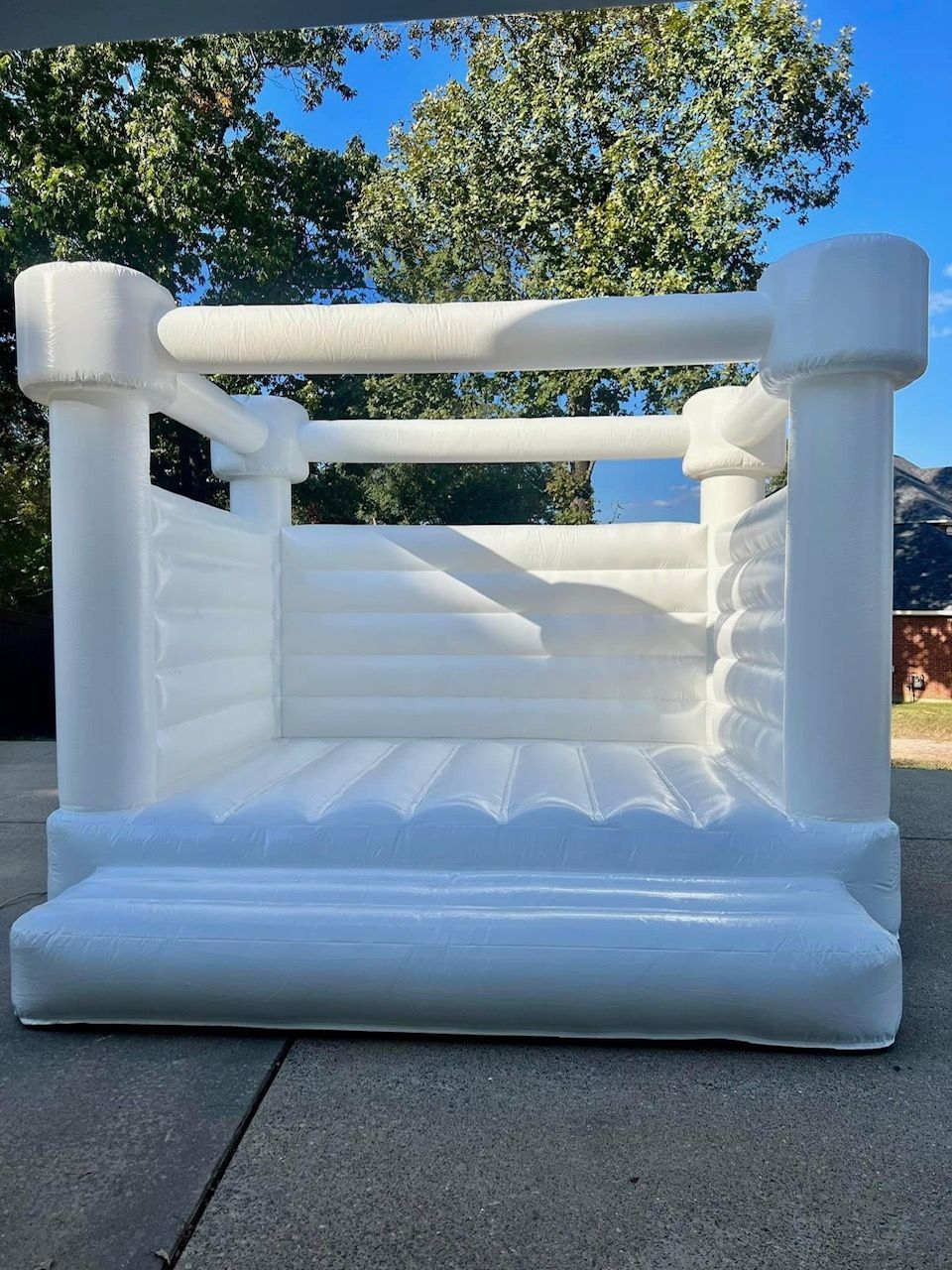 A white bouncy castle is sitting on a sidewalk in front of trees.