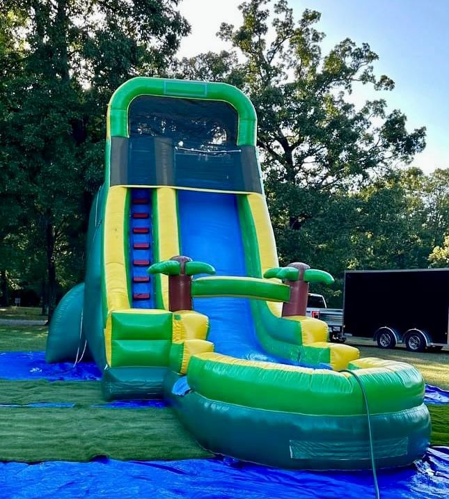 A green and yellow inflatable water slide is sitting on top of a blue tarp.