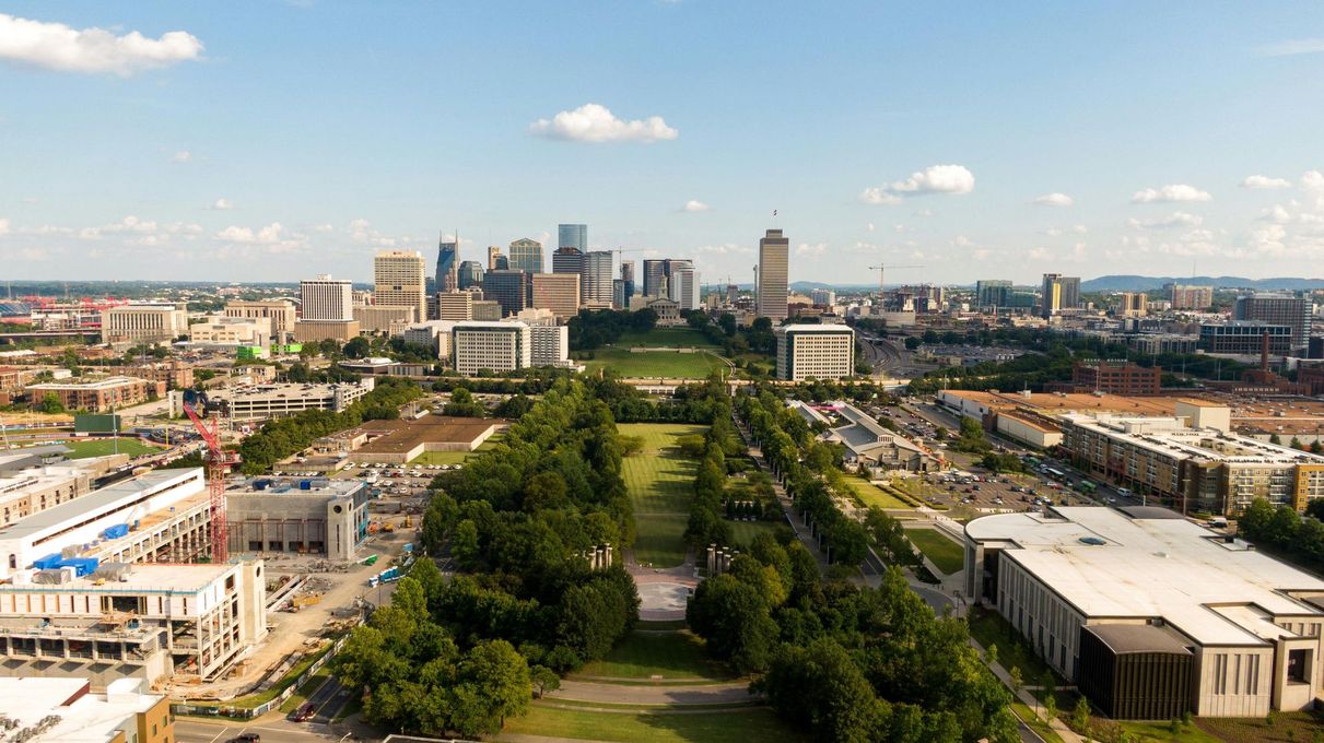 Aerial view of Nashville skyline with a long green parkway lined with trees leading toward the city center.