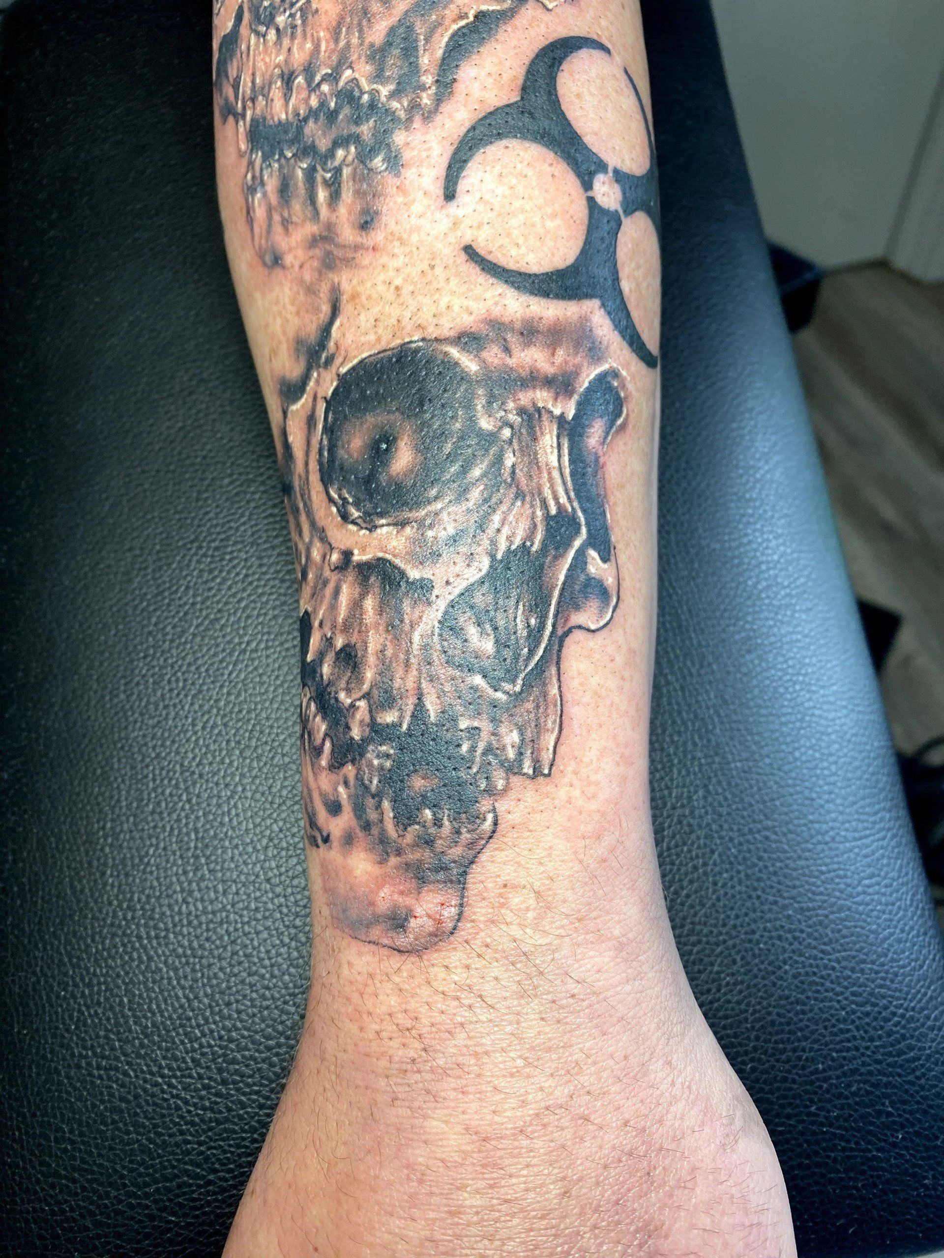 A man has a tattoo of a skull and a biohazard symbol on his forearm