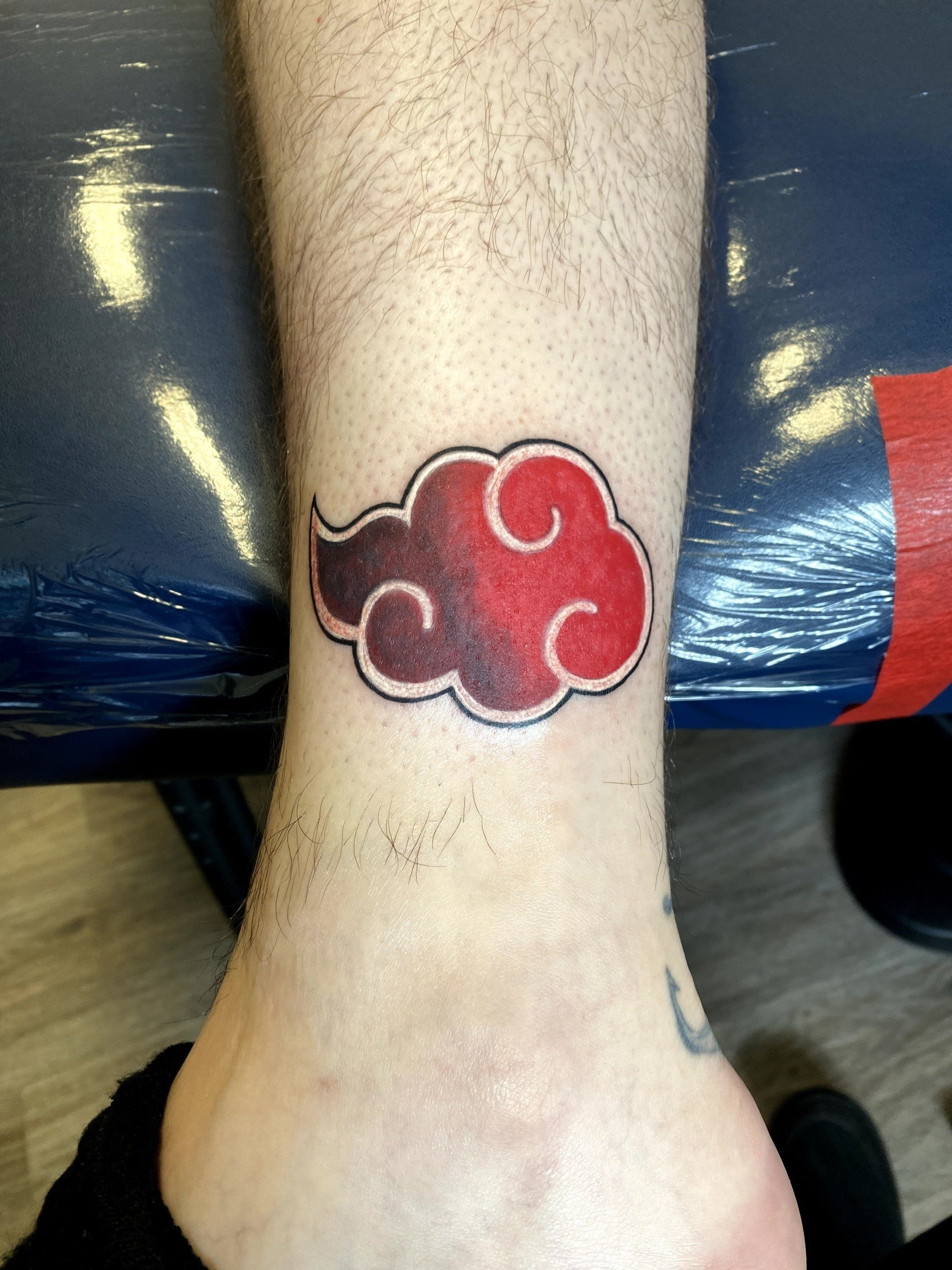A person has a red cloud tattoo on their ankle