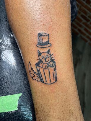 A tattoo of a cat in a trash can with a top hat.