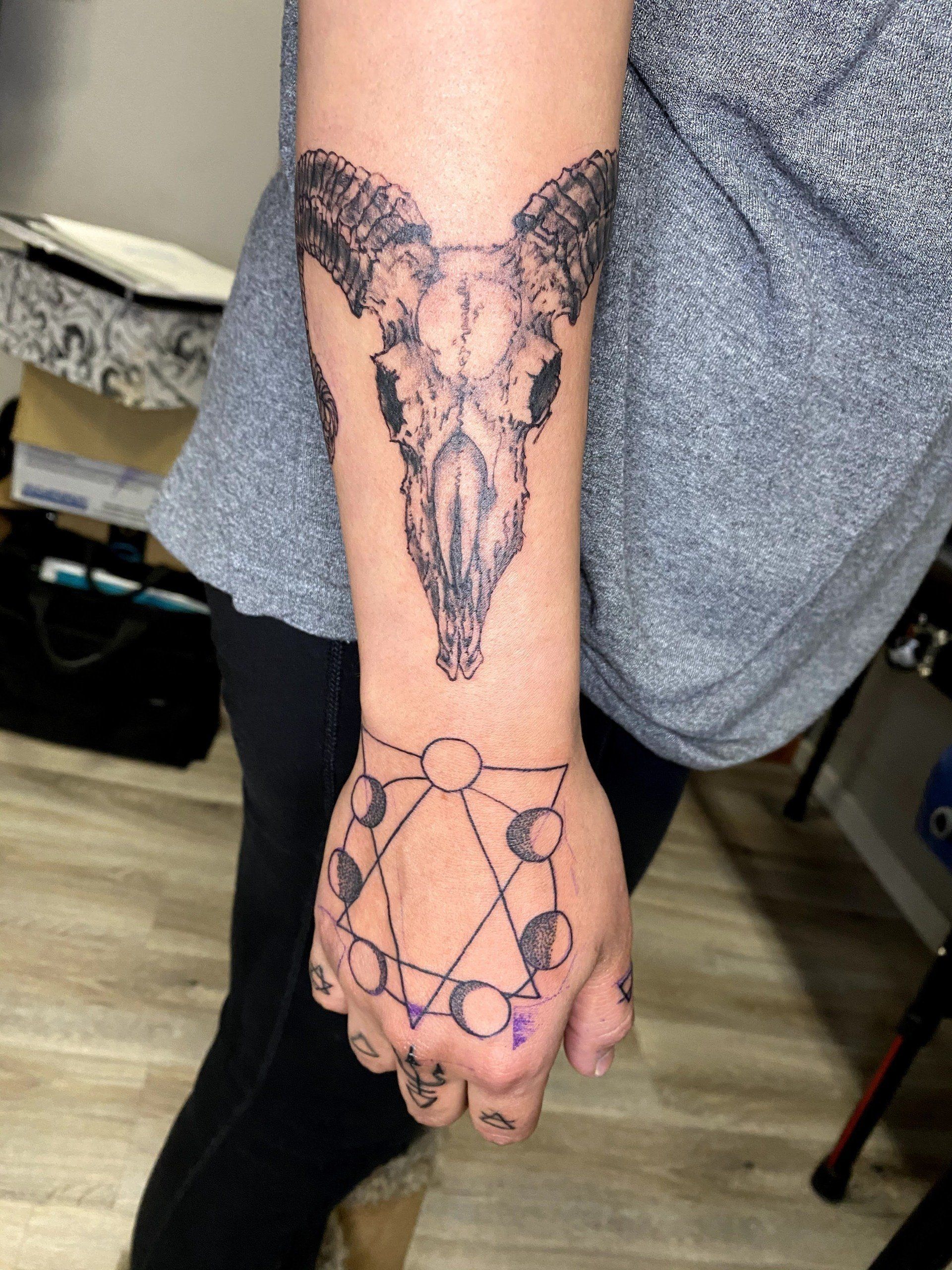 A person has a tattoo of a ram skull on their arm
