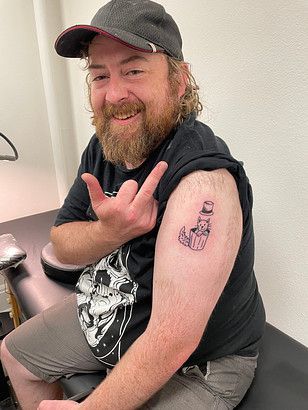 A man with a beard is getting a tattoo on his arm.