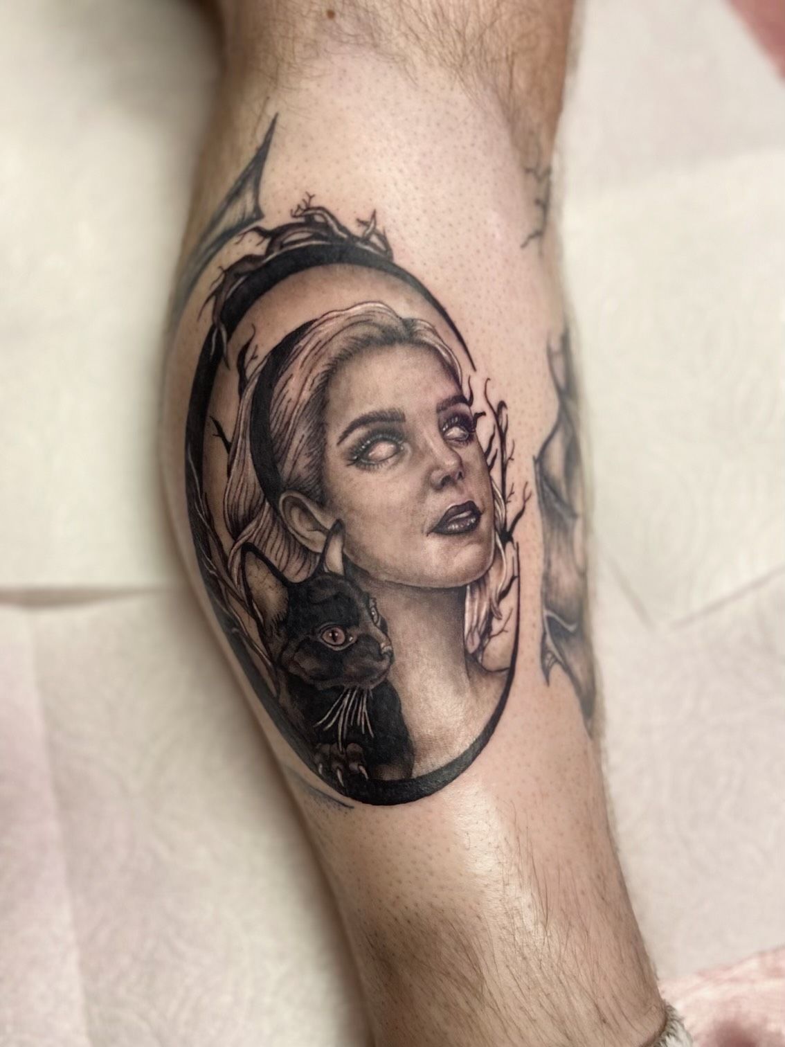 A black and white tattoo of a woman with a cat on her leg.