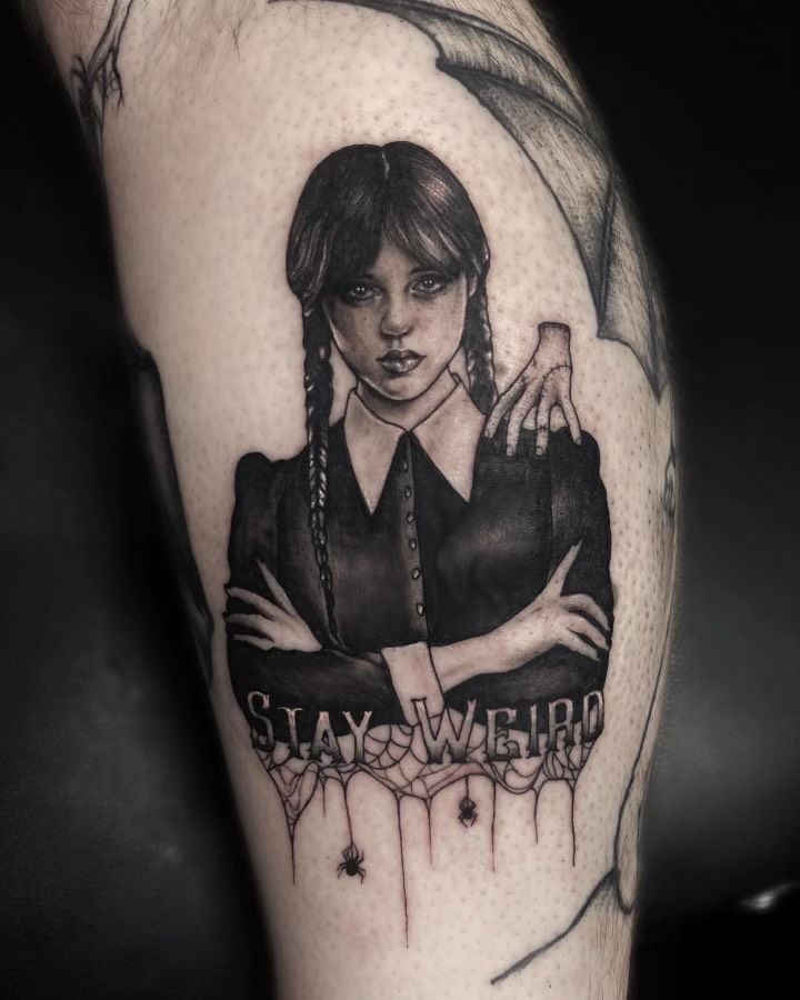 A black and white tattoo of wednesday addams on a person 's leg