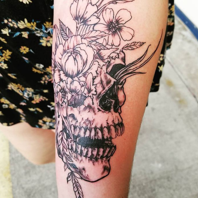 A woman has a tattoo of a skull and flowers on her arm