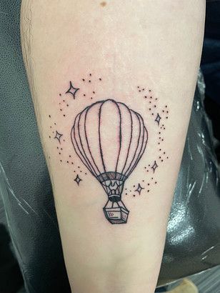 A person has a tattoo of a hot air balloon and stars on their forearm.