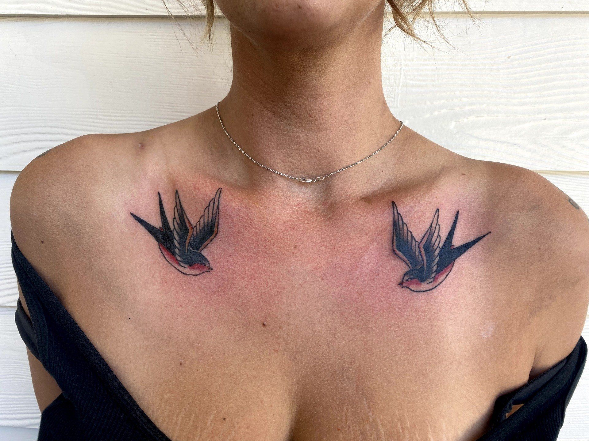 A woman has two swallows tattooed on her chest.