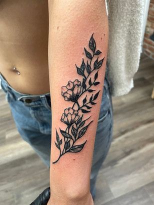 A woman has a tattoo of flowers and leaves on her forearm.