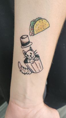 A person has a tattoo of a cat in a trash can and a taco on their wrist.