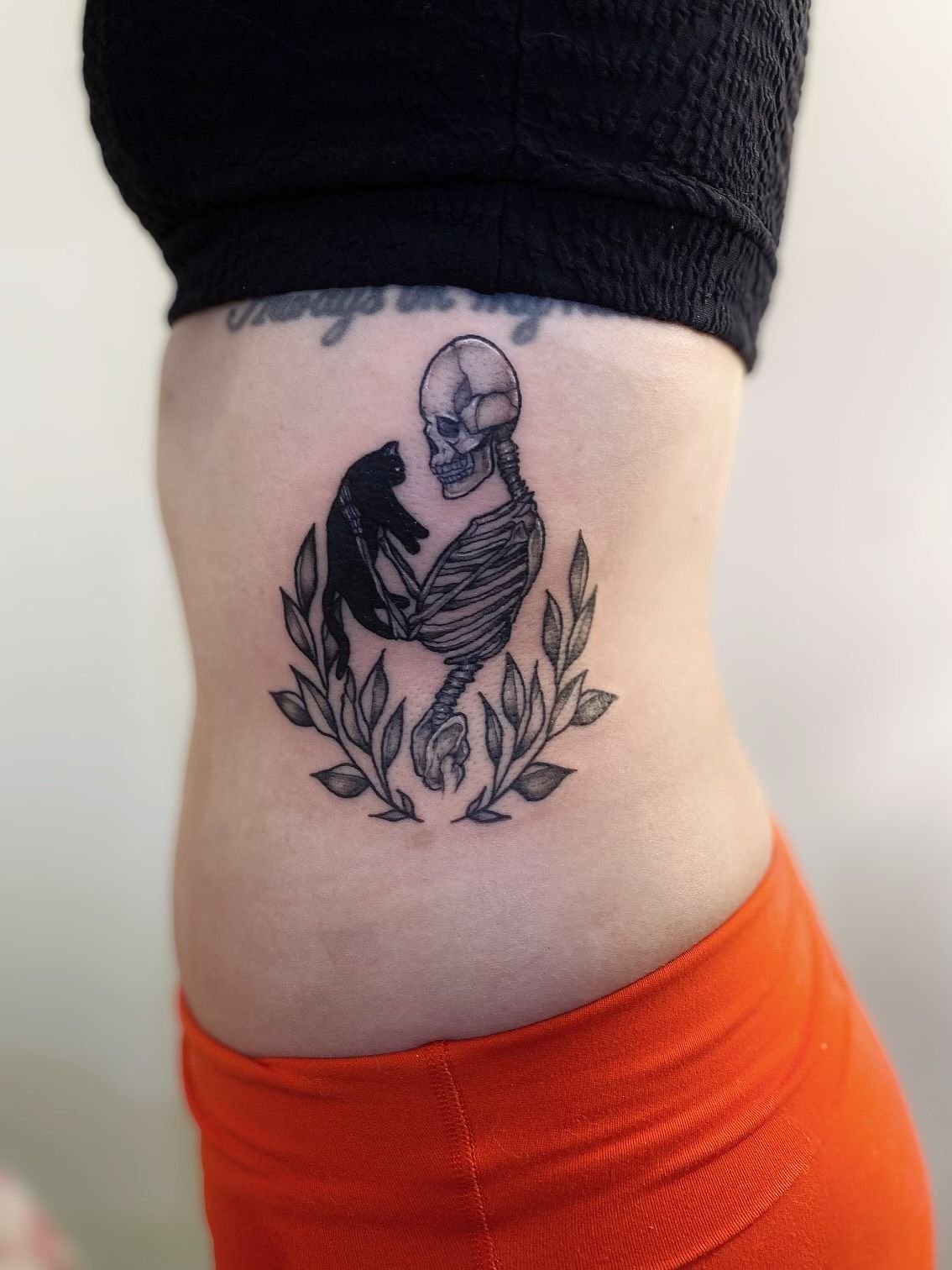 A woman has a tattoo of a skeleton holding a cat
