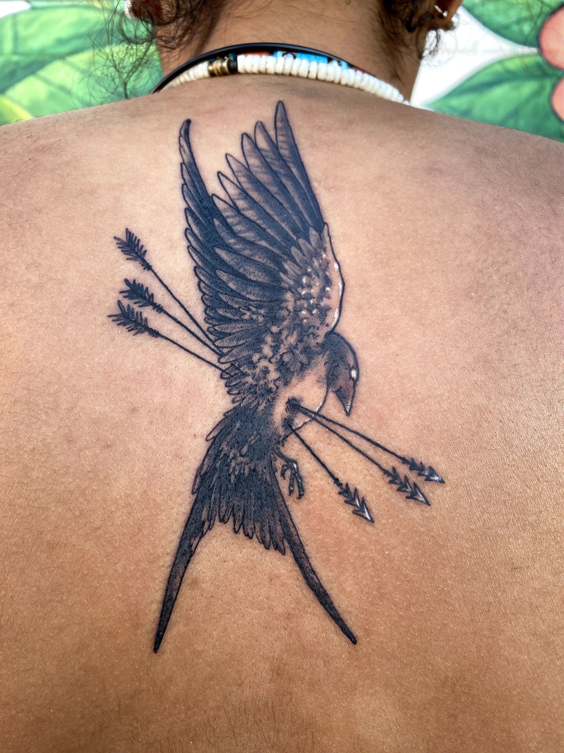 A woman has a tattoo of a bird with arrows in its beak