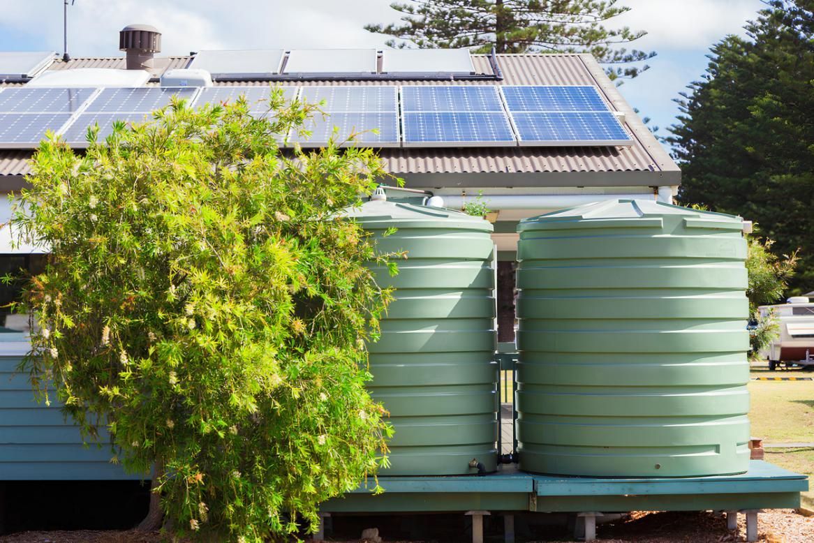 Two Green Water Tanks Are Sitting in Front of a House With Solar Panels on the Roof — V.I.P. Plastic Fabrication in Townsville, QLD