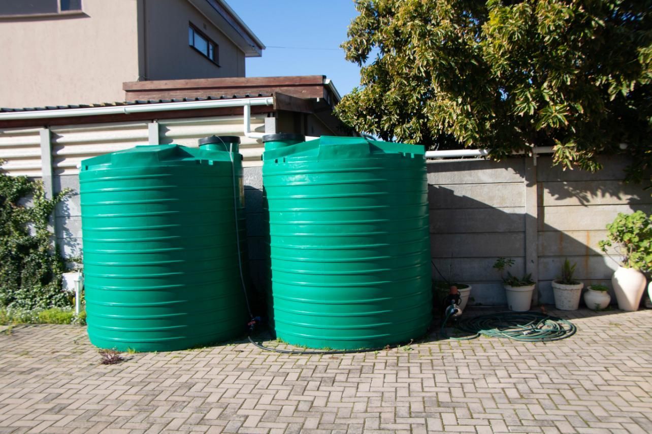 Two Green Water Tanks Are Sitting on a Brick Driveway — V.I.P. Plastic Fabrication in Cairns, QLD