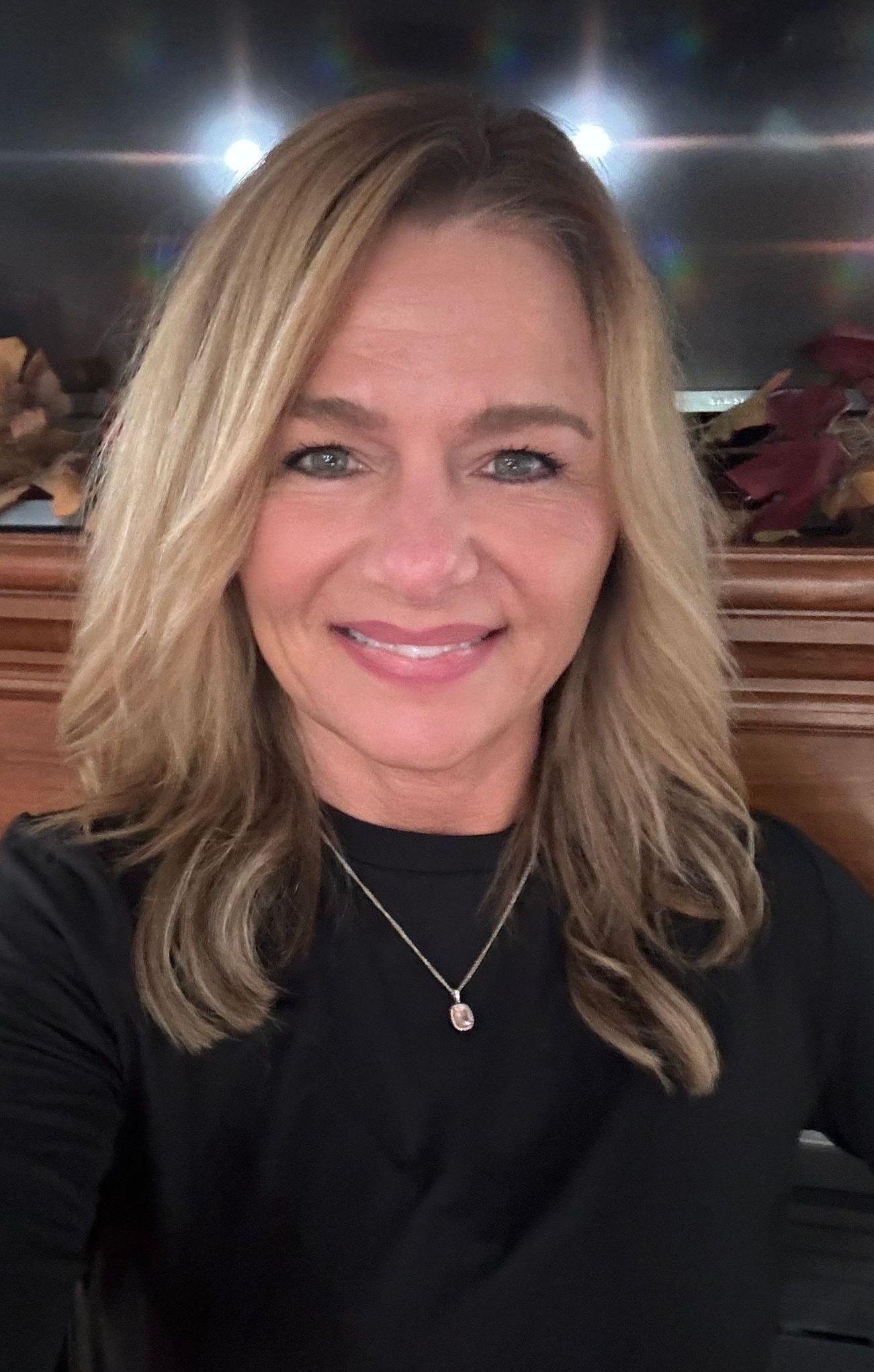 A woman wearing a black shirt and a necklace is smiling for the camera.
