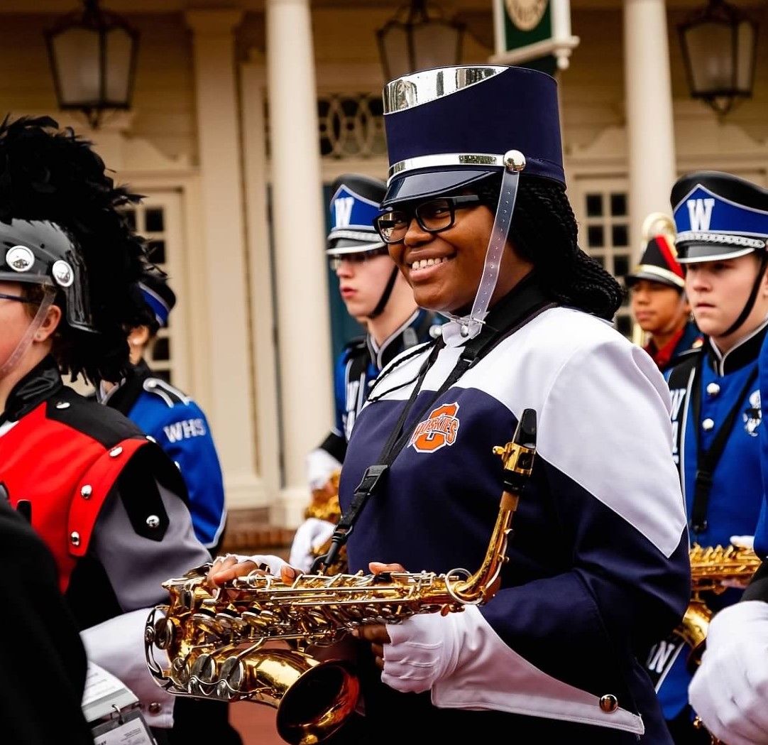 A group of marching band members in blue and red uniforms playing instruments during a parade.