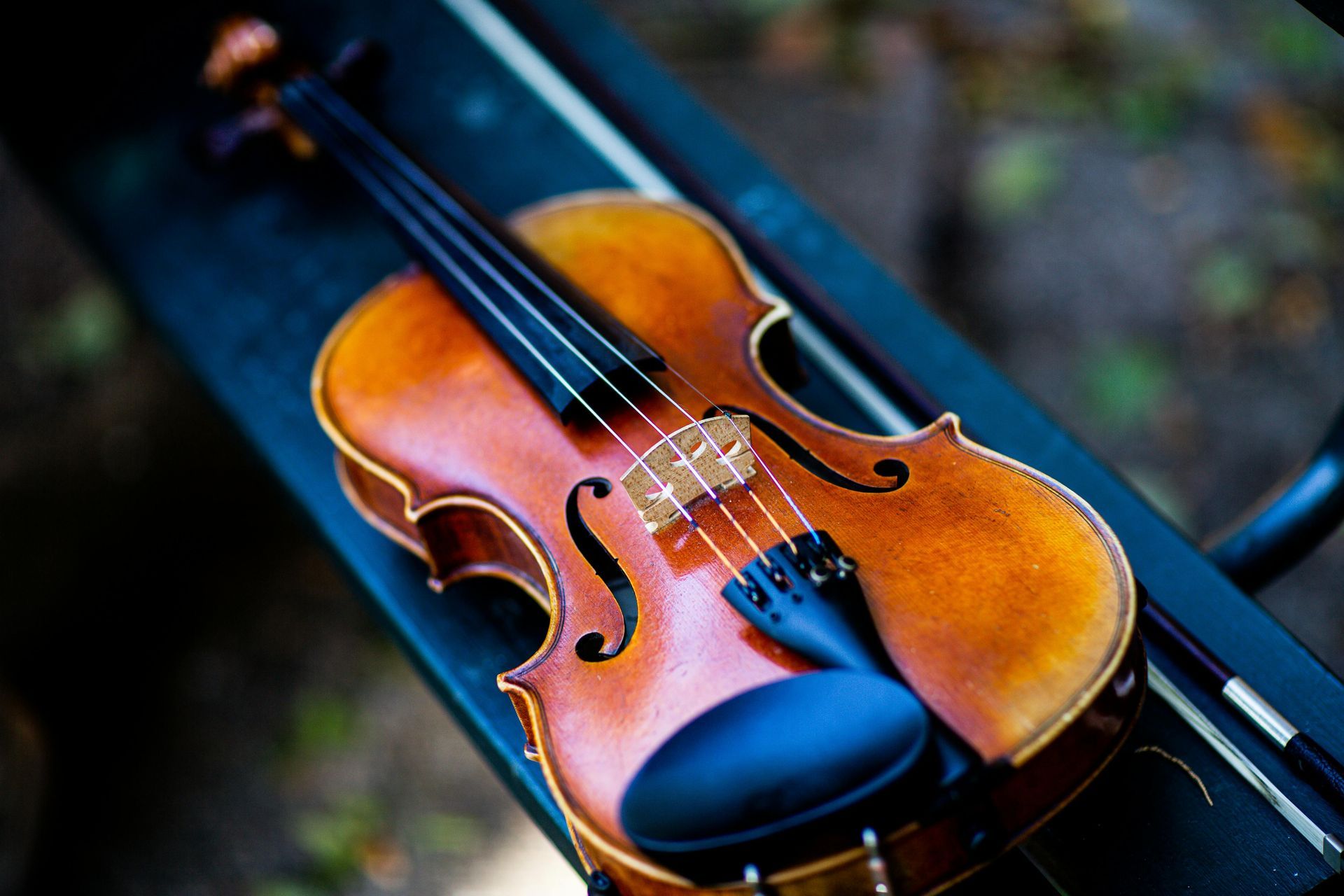 A wooden violin resting on a dark, outdoor bench with its bow lying beside it.