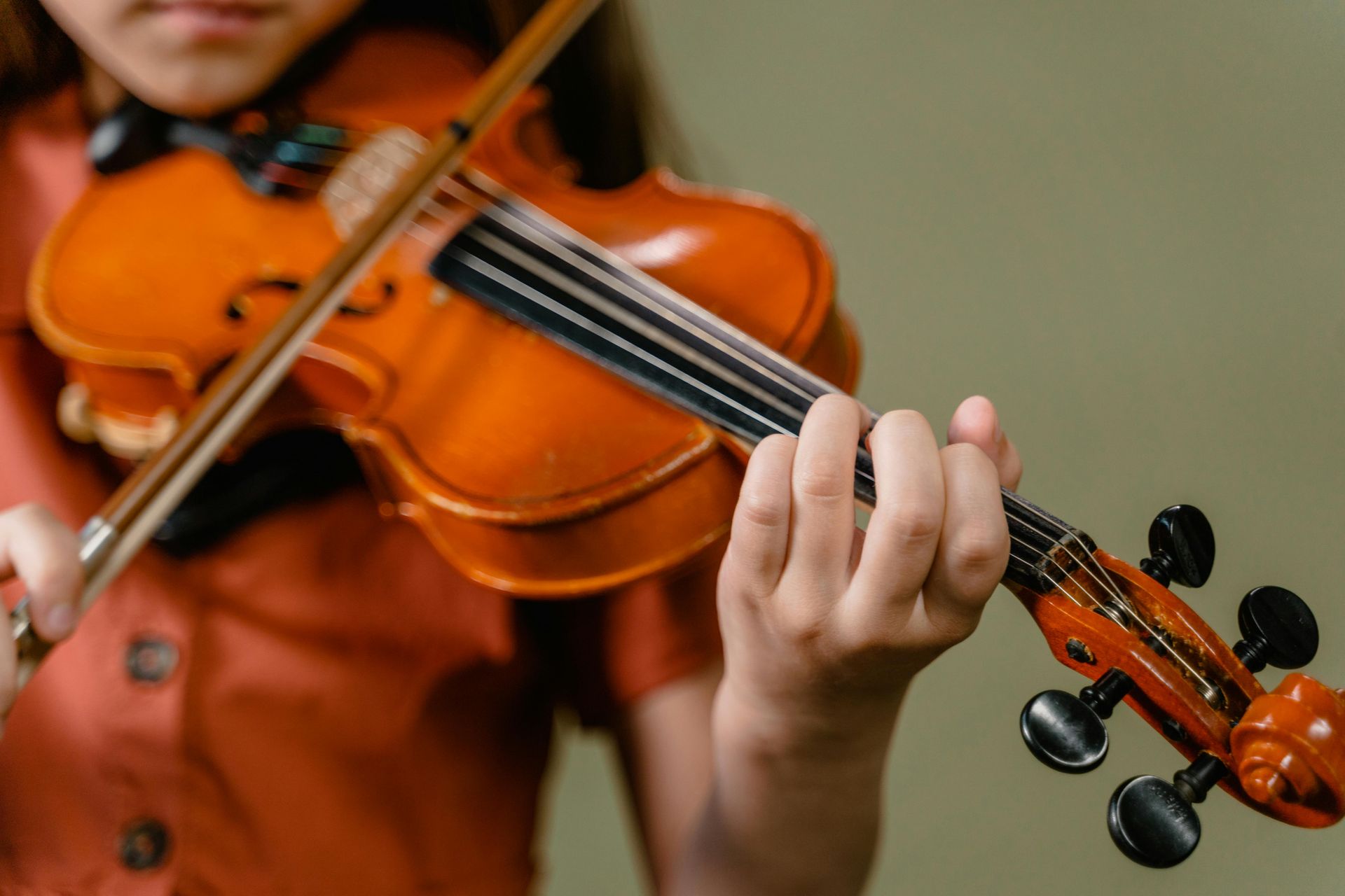 A person playing a wooden violin against a plain background.