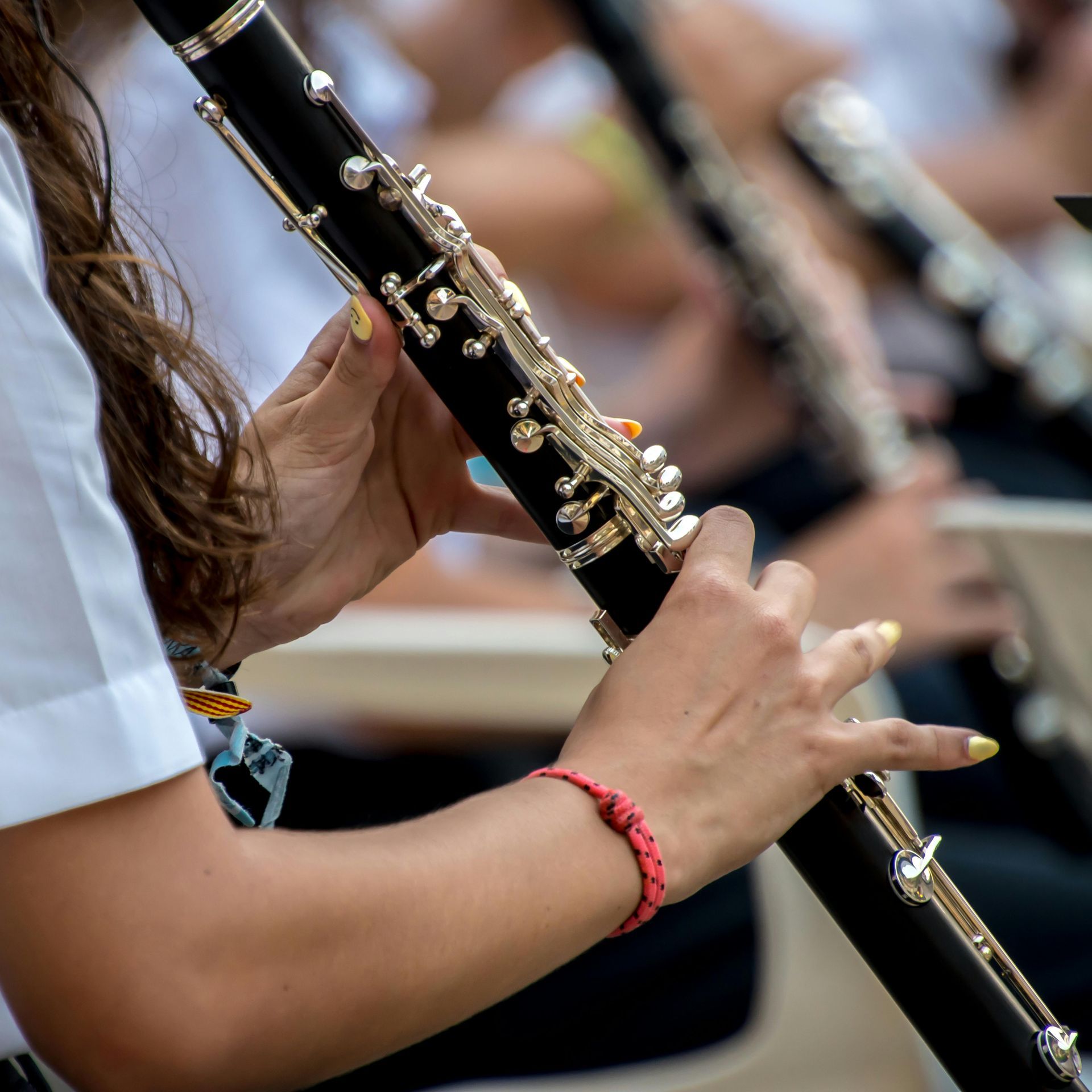 Close-up of a musician's hands playing a clarinet in an orchestra setting, showing fingers on the metal keys.