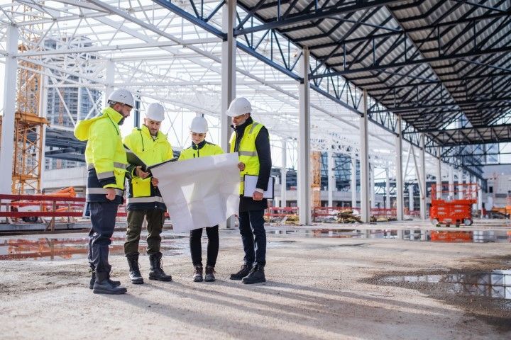 Construction workers reviewing blueprints at a construction site, wearing safety vests and hard hats.